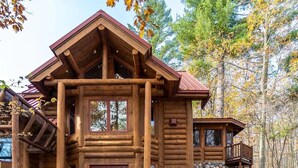 A log cabin with a stone foundation, large windows, and a porch with outdoor seating. - Redstone, a one-of-a-kind, luxurious 7200 sq. ft. impressive Lakeside log home (Land O' Lakes)