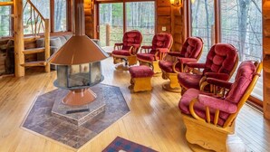 A log cabin interior with a fireplace, multiple red upholstered chairs, and large windows offering a forest view. - Redstone, a one-of-a-kind, luxurious 7200 sq. ft. impressive Lakeside log home (Land O' Lakes)