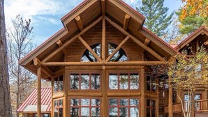 A log cabin with a large front porch, stone foundation, and multiple windows. - Redstone, a one-of-a-kind, luxurious 7200 sq. ft. impressive Lakeside log home (Land O' Lakes)