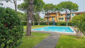 A swimming pool surrounded by greenery, with a building in the background. - Sirmione Studio Apartment (Sirmione)