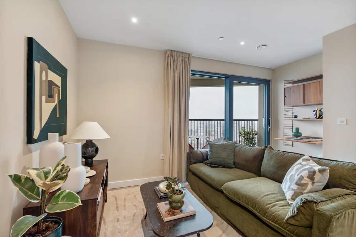 Een moderne woonkamer met een bank, een salontafel en een lamp. Er is uitzicht op een balkon met een balustrade.