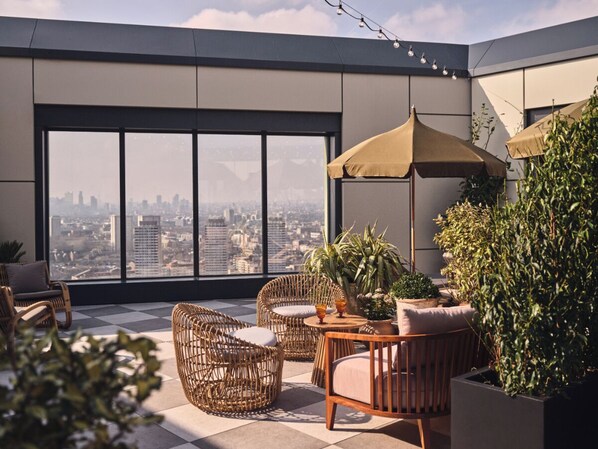 A rooftop terrace with wicker furniture, potted plants, and a view of the cityscape.