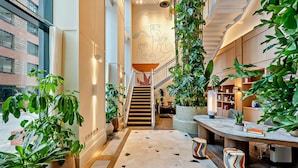 A modern interior with a staircase, potted plants, and a wooden desk area. - Riverstone Heights (London)