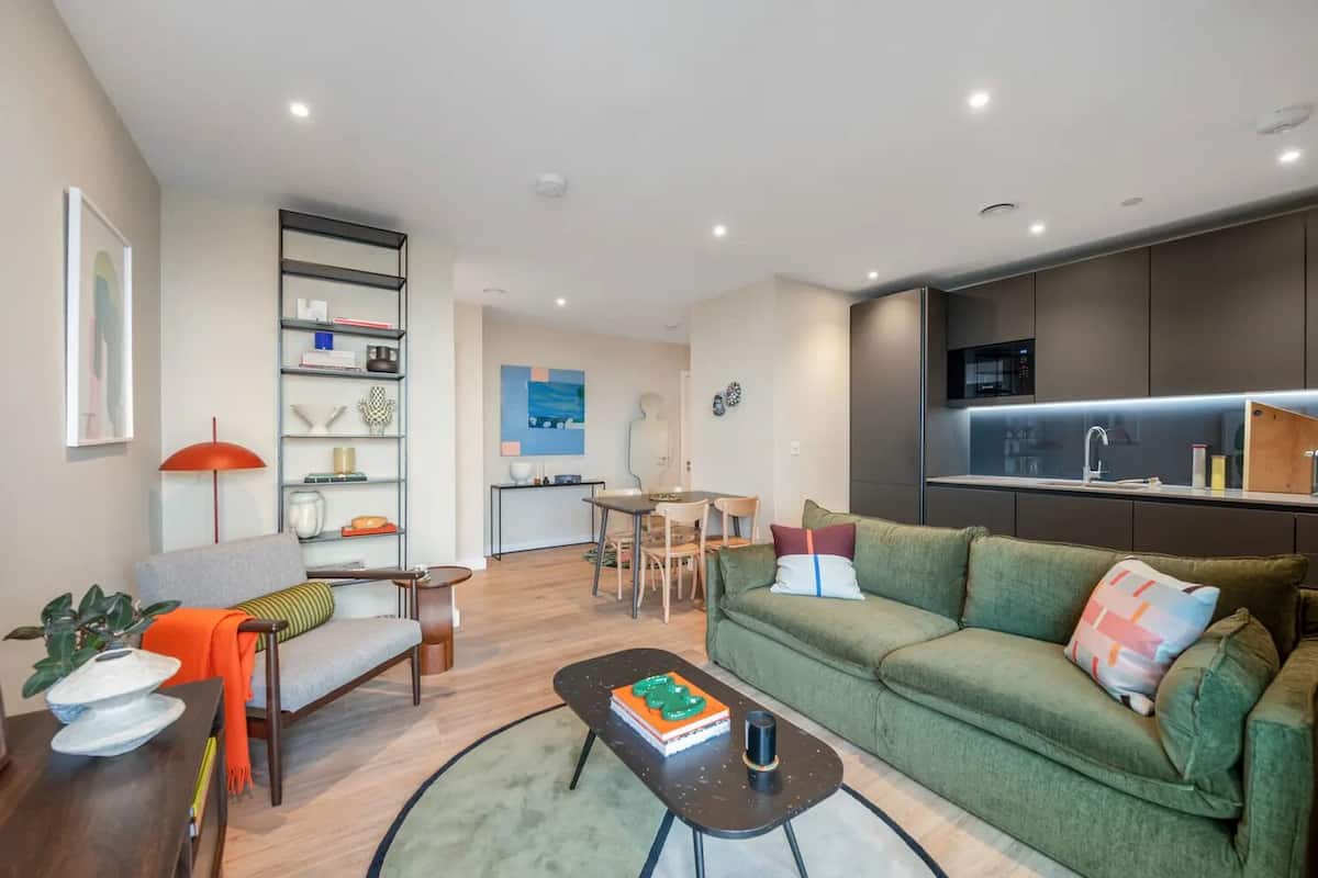 Een moderne woonkamer met een groene bank, een salontafel en een eethoek met een tafel en stoelen.