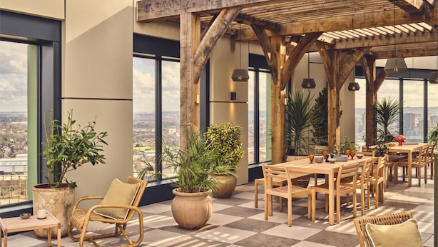 A rooftop terrace with wooden furniture, large potted plants, and a city view. - Riverstone Heights (London)