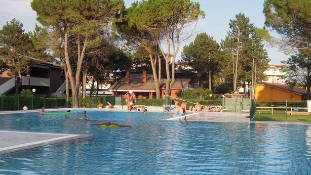 Piscina com pessoas, rodeada por árvores e edifícios.
