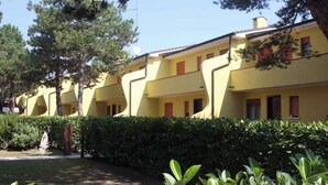Uma fileira de edifícios amarelos com persianas vermelhas, cercada por vegetação e árvores.