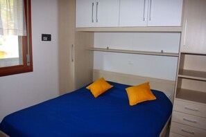 A bedroom with a bed, two yellow pillows, a window with blinds, and a wardrobe with multiple compartments.