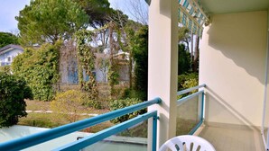 A balcony with a table and chairs, a railing, and a view of a building with trees and a fence.