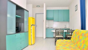 A compact living space with a kitchenette, a sofa, and a yellow refrigerator.
