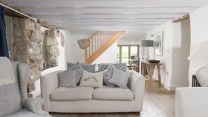 A cozy living room with a stone wall, a wooden staircase, and a view to the dining area. - Fairings -  a house that sleeps 8 guests  in 4 bedrooms (St Ives)