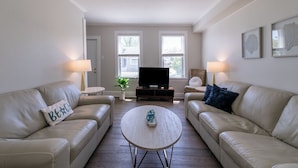 Un salon avec deux canapés en cuir beige, une table basse ronde, un téléviseur à écran plat et deux lampes.