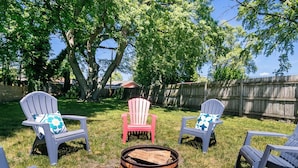 Un jardin avec quatre fauteuils Adirondack, dont un avec un dossier rouge, disposés autour d’un foyer central.