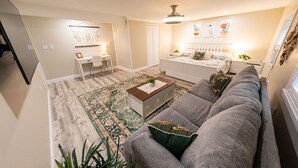 A modern living room with a grey sofa, a small white desk, a bed with a white headboard, and a large decorative rug. - Extra large 1 Bedroom apartment! (Salem)