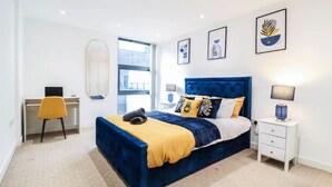 A modern bedroom with a large bed, a desk, and a chair. - 1 Bed Canary Wharf Flat (Greater London)