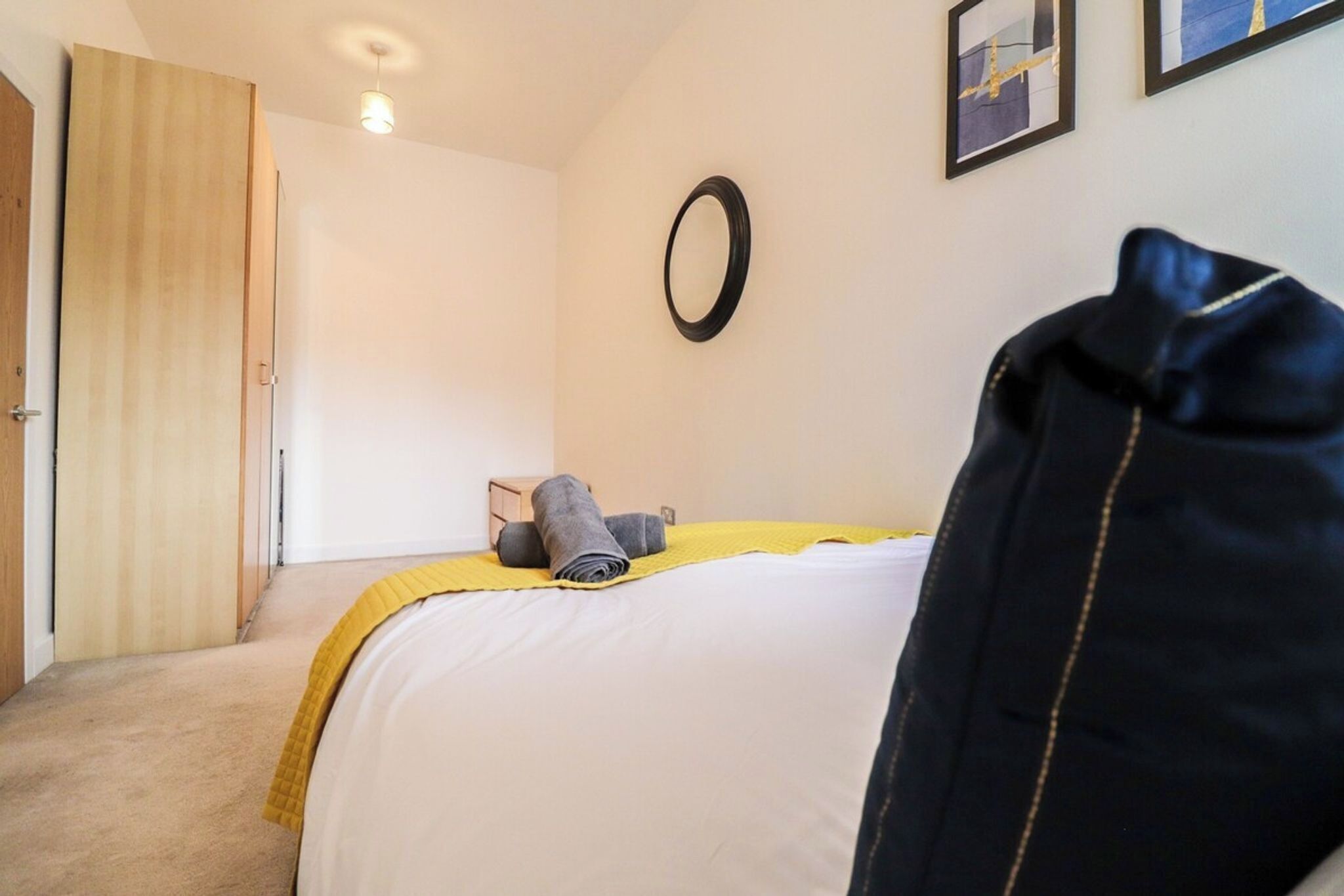 A bedroom with a bed, a door, a wall-mounted mirror, and a small wooden box.