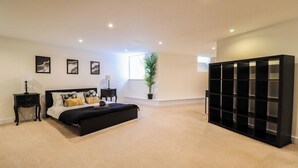 A bedroom with a bed, a nightstand, a potted plant, a bookshelf, and a window. - Huge London 2 Bed Flat w/Parking (Greater London)