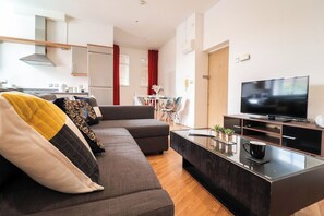 Un salon moderne avec un canapé, une table basse, un téléviseur et un coin cuisine à l’arrière-plan.