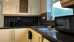 A kitchen with white cabinets, a black tiled backsplash, a microwave, and a window providing natural light.