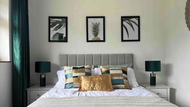A neatly made bed with a patterned bedspread, two bedside tables with lamps, and three framed pictures on the wall.