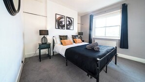 Een slaapkamer met een bed, twee nachtkastjes, een lamp, een radiator en een raam met gordijnen.