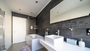 Een moderne badkamer met een bad, een grote spiegel en een witte wastafel.