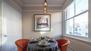Een eetgedeelte met een ronde tafel, twee stoelen, een lijst met kunstwerk en een raam met uitzicht op gebouwen.