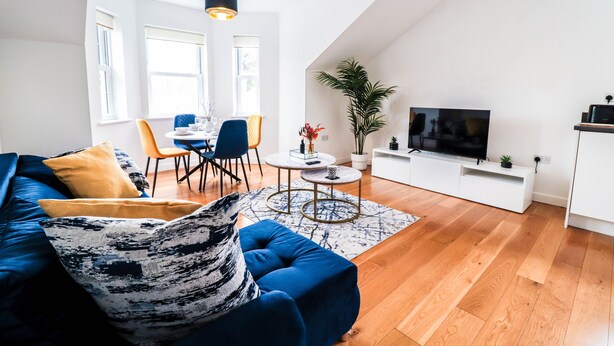Ett modernt vardagsrum med en blå soffa, en matplats med stolar, en tv och en växt.