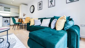 Una sala de estar moderna con un sofá azul aguamarina, una mesa de comedor con sillas y una cocina al fondo.