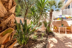 A patio area with a table and chairs, surrounded by various plants and a colorful umbrella. - Sardinia RE - Al Porto (Alghero)