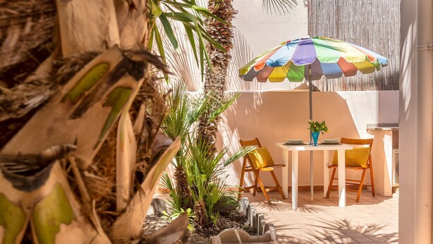 An outdoor patio with a table and chairs, surrounded by plants and a colorful umbrella. - Sardinia RE - Al Porto (Alghero)