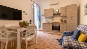 A compact kitchen with a dining area, a sofa, and a TV. - Sardinia RE - Al Porto (Alghero)