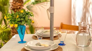 A table set with plates, cutlery, a glass pitcher, and a blue vase with a plant. - Sardinia RE - Al Porto (Alghero)