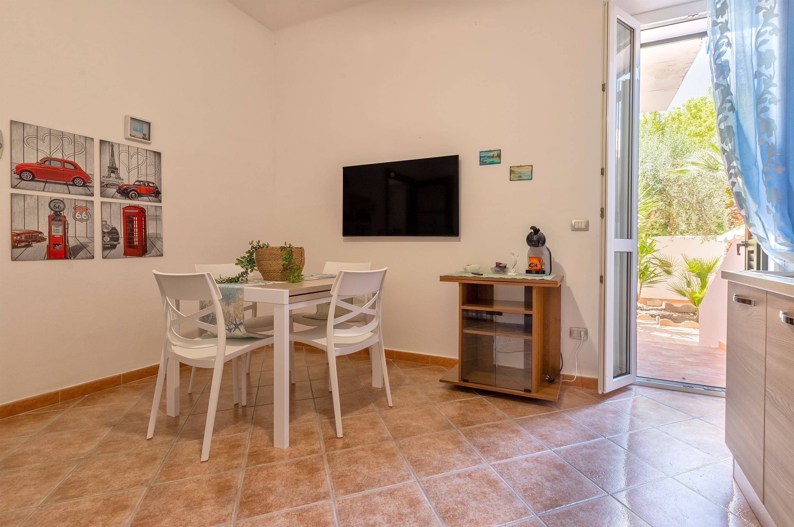 A dining area with a table and chairs, a flat-screen TV mounted on the wall, and a small cabinet with a plant.