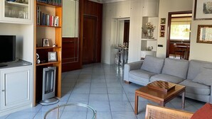 Ein Wohnzimmer mit einer Couch, einem Couchtisch und einem Fernseher. Es gibt Bücherregale und einen Kamin.