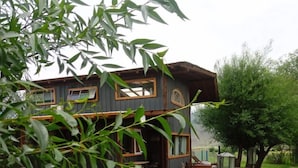 Eine rustikale Holzhütte mit einer Holzterrasse, umgeben von viel Grün und einem Baum.
