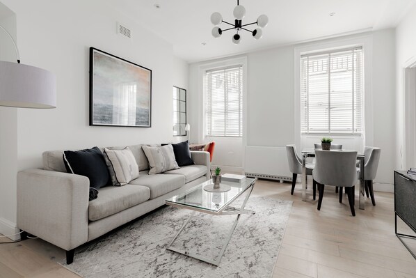 A modern living room with a sofa, coffee table, dining table, and chairs. - Marylebone by Excel Apartments (London)