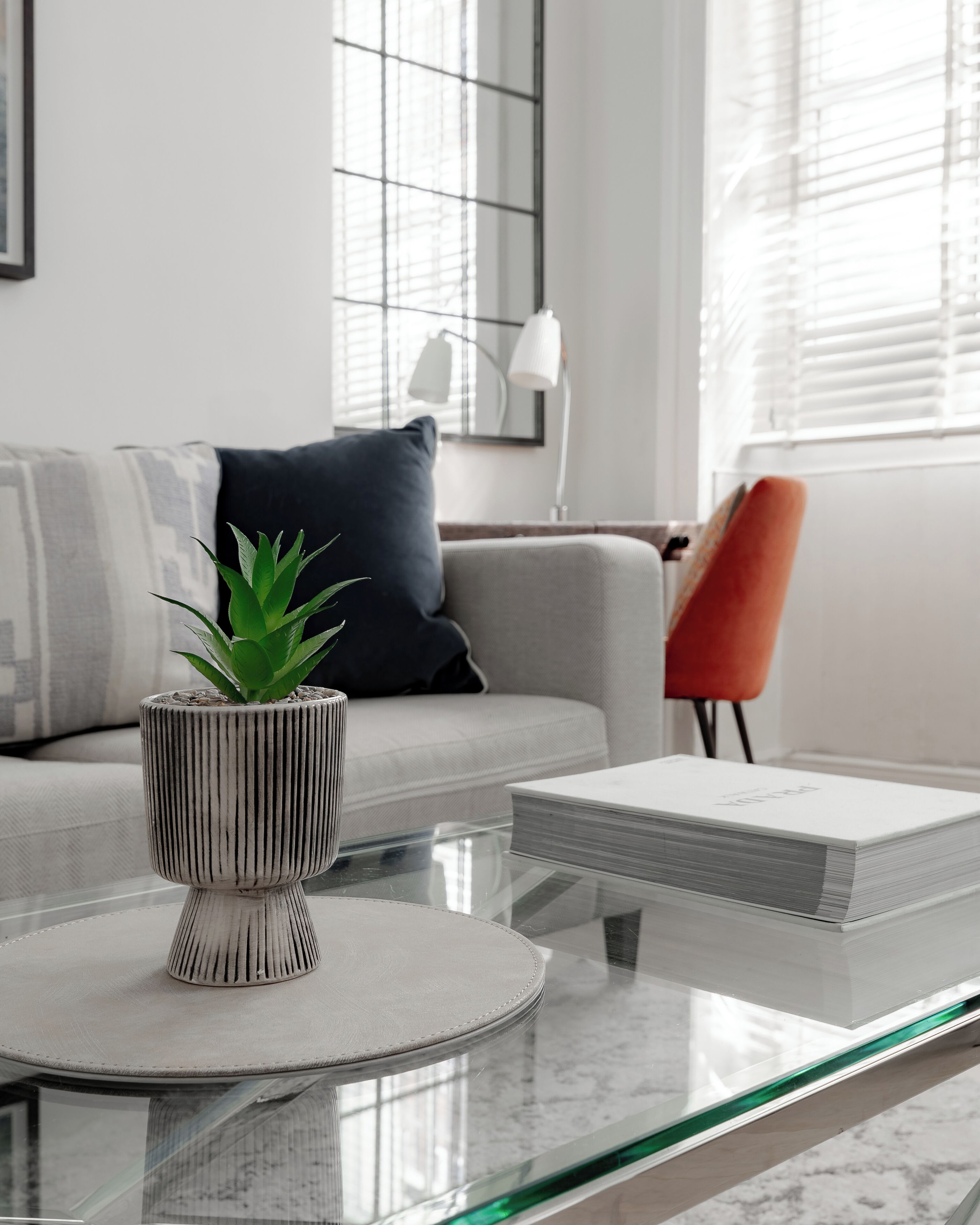 Un salon moderne avec une table basse en verre, une plante en pot, un canapé avec des coussins, un fauteuil rouge et une lampe.