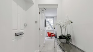 Un corridoio moderno con un tavolo in vetro e orchidee bianche, che conduce a una stanza con una poltrona rossa e una finestra.