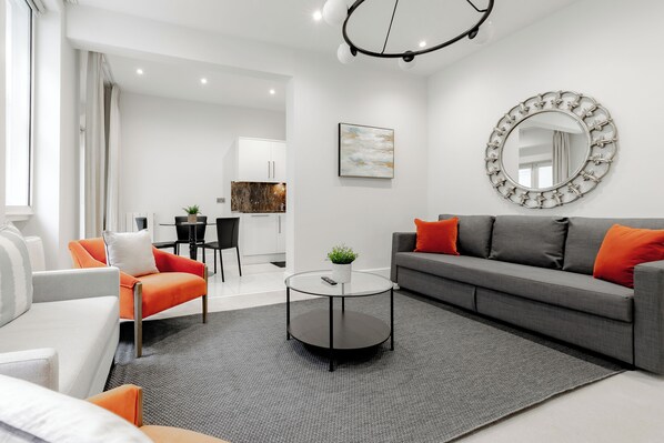 A modern living room with a grey sofa, orange cushions, a round coffee table, and a large mirror. - Marylebone by Excel Apartments (London)