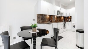 Una cucina moderna con mobili bianchi, un piano di lavoro in marmo e un'area pranzo con tavolo e sedie neri.