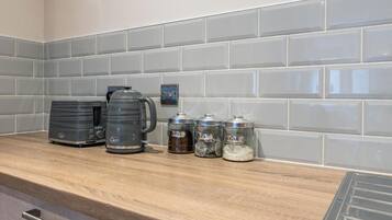 A kitchen counter with a coffee maker, a kettle, and three spice jars labeled coffee, tea, and sugar.