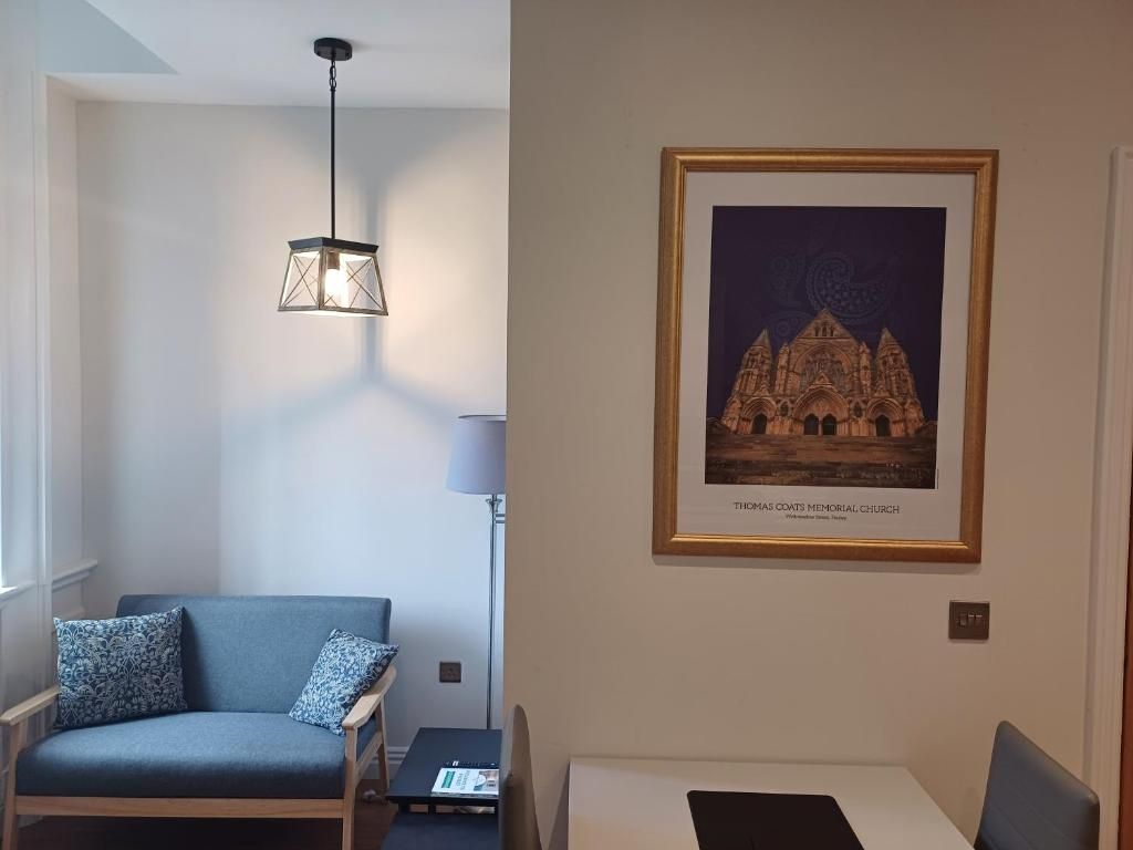 Una habitación con un sofá azul, una mesa, un cuadro enmarcado de una catedral y una lámpara colgante.