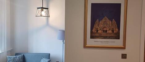 A room with a blue sofa, a table, a framed picture of a cathedral, and a hanging light fixture.