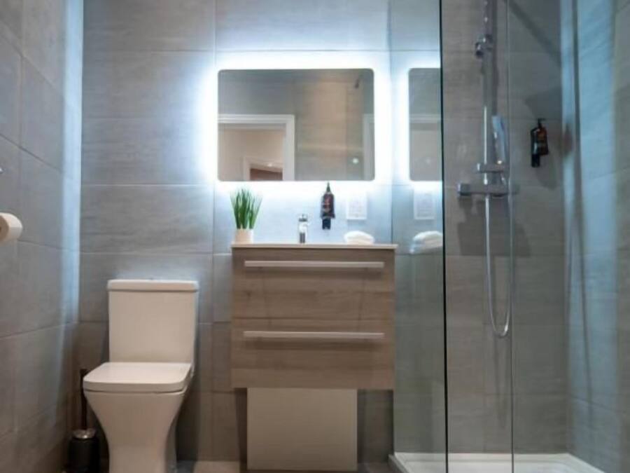 Un baño moderno con cabina de ducha de vidrio, inodoro y tocador con espejo.