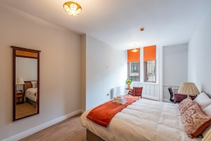 Habitación de hotel con una cama grande, un espejo, una ventana con persianas naranjas, un escritorio con lámpara y una silla.