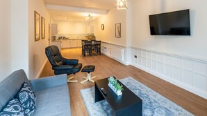 A modern living room with a sofa, a coffee table, and a TV mounted on the wall. - The Hazlitt Apartments (Paisley)