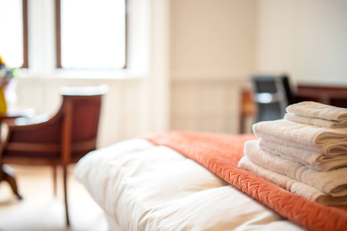 A neatly made bed with a white comforter and an orange throw blanket.