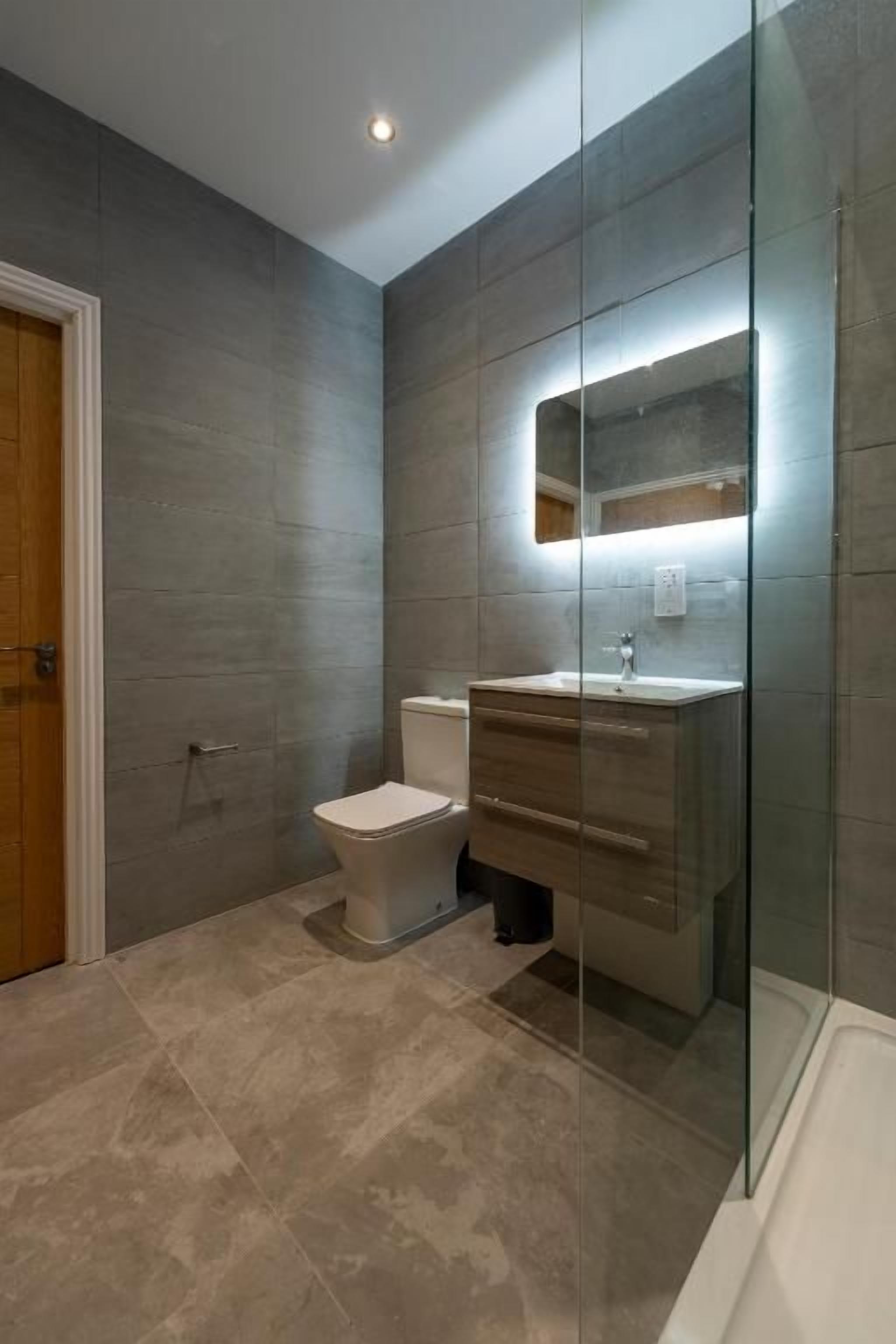 Une salle de bain moderne dotée d’une douche à parois de verre, de toilettes et d’un meuble-lavabo avec un miroir.