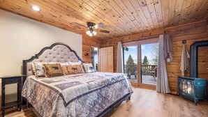 Camera da letto in una baita di legno con un letto grande, una ventola a soffitto e un camino a legna.